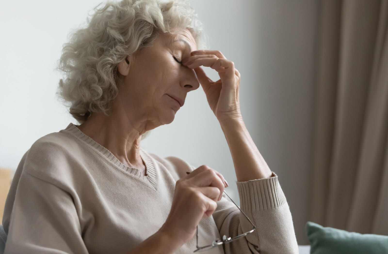 An older adult rubs her eyes while holding her glasses, appearing to experience vision discomfort.